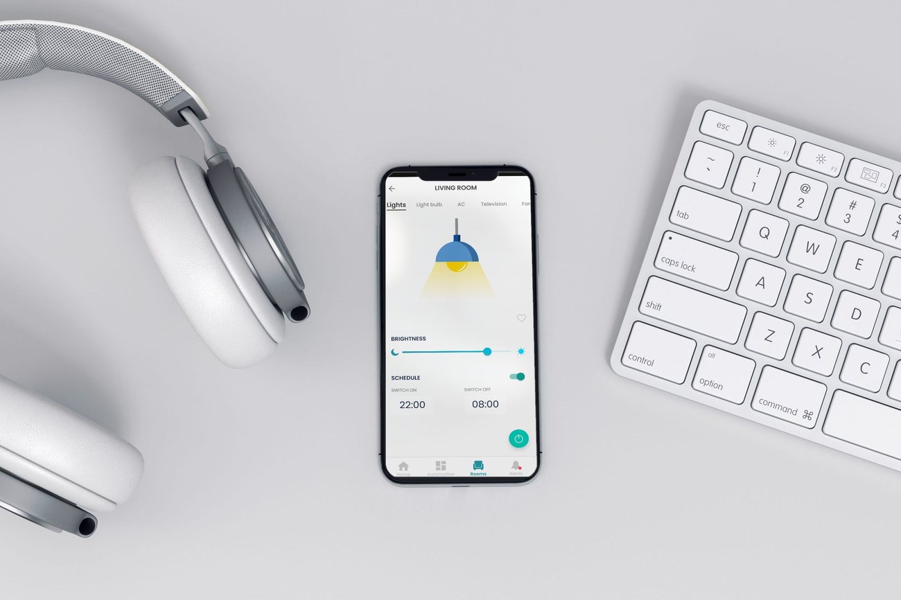 Vitae 22 app on a phone in a desk flatlay: a Living Room lights screen with a pendant lamp, brightness slider, and an on/off schedule